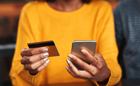 Image containing a woman holding a credit card and a mobile phone