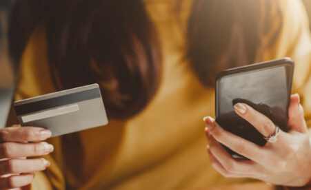 Image containing a woman holding a credit card and a mobile phone