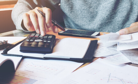 Image containing a person at a desk with a pen and calculator